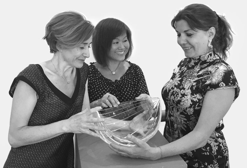 Raffaella Fossati, Marta Comini e Kinue Horikawa posano insieme con un centrotavola della collezione di cristalli Sheer Nature di Angelo Mangiarotti